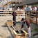 A tour group stands around a shallow dirt pit watching a re-enactment of 2 prospectors panning for gold